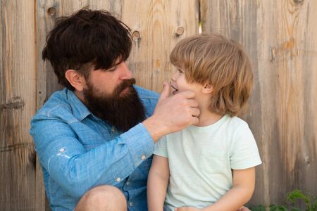 Father checks the teeth of his son. Care for baby teeth. Dad and boy are sitting near the fence. Caring father. Familyの写真素材