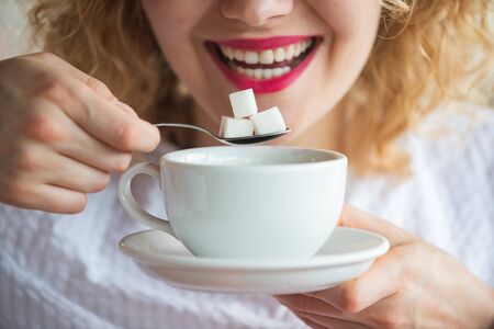 Woman holds sugar cubes. Blood sugar, insulin, health. Beautiful woman with a cup of sweet coffee.の写真素材