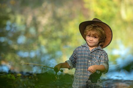 Happy child. American boy. Kid in a hat holds a fishing rod and smiles. Weekend on the lake.
