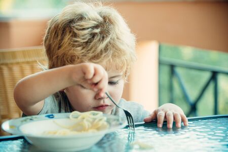 Child and food. Childrens appetite. Baby child eating spaghetti at table.の写真素材