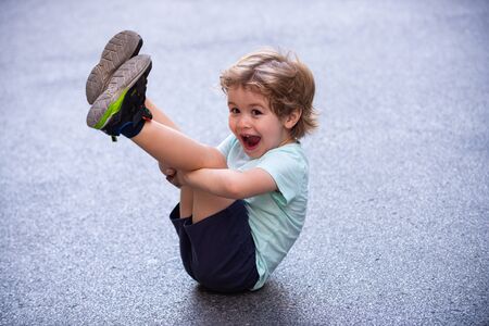 Happy funny child. Cute kid sits on the pavement. Happy child portrait. Childhood on the asphalt road or pavement. The child of the city. Urbanization and children. Fun summer holidays in big city.の写真素材