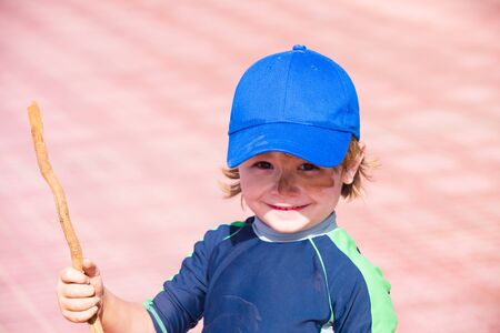 Camouflage Face Paint. Boy with a stick plays in the military. Games on the street. Childhood in summer. Happy child with a dirty face and a stick.の写真素材