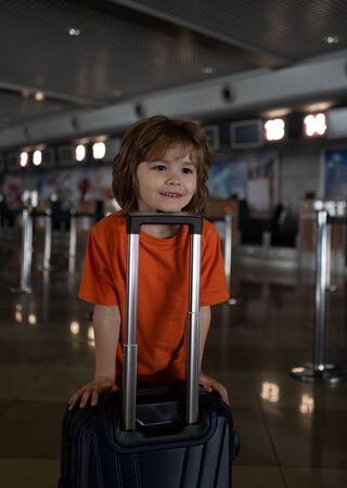 Happy funny boy in the empty airport. Traveling during the Covid 19, coronaviruse. Travel and tourism. Attractive boy with hand luggage for flight to USA.の写真素材
