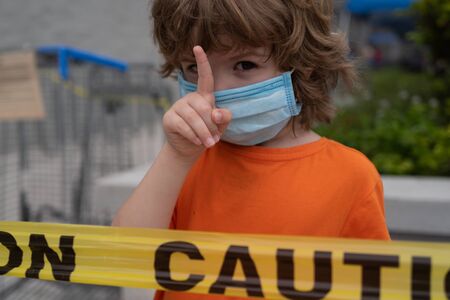 Cute child in the mask shows a warning sign during coronavirus