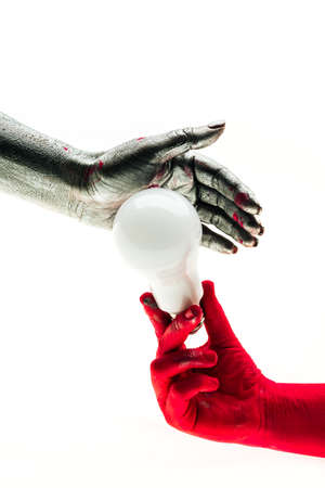 Energy bulb alternative. Beautiful multi-colored hands hold white electric bulb, red and silver hand. Alternative energy, resources, energy sources for the planet for people. Hands holding LED bulbの写真素材