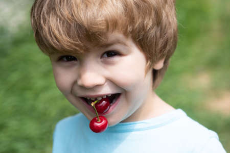 Cute boy with cherries in his mouth. Healthy food with natural vitamins.の写真素材
