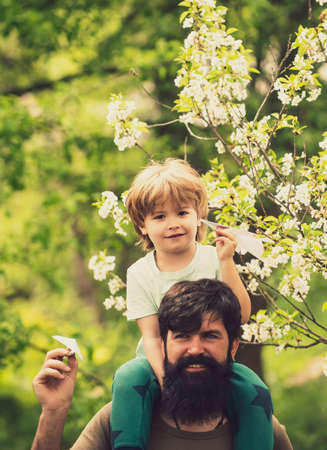 Small boy is sitting on his fathers shoulders. Beautiful spring family concept. Son and dad, friendship. Family walk.の写真素材