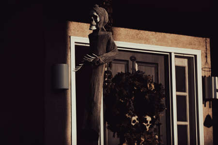 Scenery for Halloween in October. Decoration in the yard. Autumn wreath with a human skull skeleton on the front door of the house.の写真素材