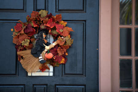 Witch on a broom. Autumn wreath on the front door with flowers. Scenery for Halloween in October. Decoration in the yard.の写真素材