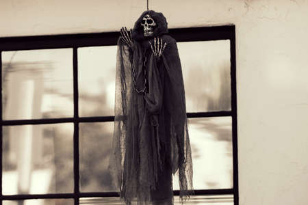 The skeleton of death hangs at the window of the family home. Scenery for Halloween in October. Decoration in the yard.の写真素材