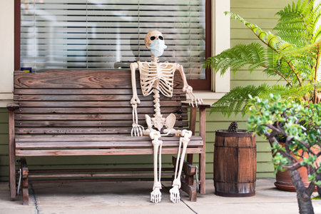 Skeleton in mask on the bench, coronavirus pandemic. Scenery for Halloween in October. Decoration in the yard.の写真素材