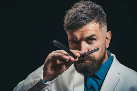 Beard styling and cut. Bearded client visiting barbershop. Barber scissors and straight razor. Brutal guy.の写真素材