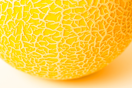 A piece of round yellow melon on a white surface. Texture. Melon skin close up. Shallow DOF, selective soft focus.の写真素材