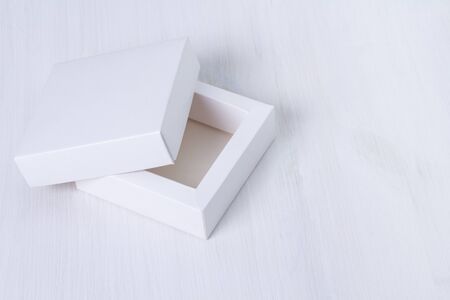 Open empty white gift box with a lid on isolated wooden background. Side view, square box. Elegant eco-friendly mockup. Isolated cardboard box with cover on white table. Empty space on the right.の写真素材