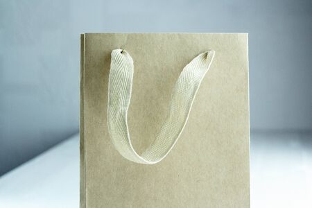 Disposable small craft paper bag for takeaway on white table in the interior. Packaging template mock up. Handle made of natural materials. Part of the package. Cool colors. Place for text.の写真素材