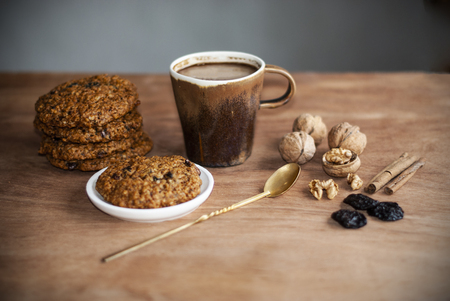 oatmeal cookies, brown mug with cocoa, walnuts, cinnamon, prunes, vintage spoon on the wooden tableの写真素材