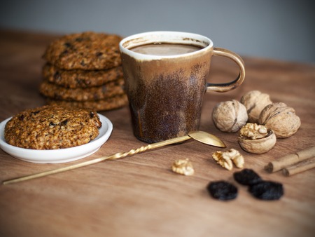 oatmeal cookies, brown mug with cocoa, walnuts, cinnamon, prunes, vintage spoon on the wooden tableの写真素材