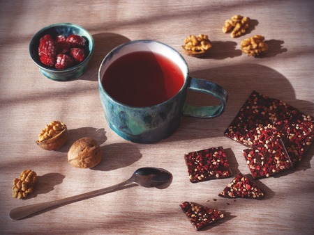 Hot tea and homemade chocolate with nuts and raspberries on wood background, slightly top viewの写真素材