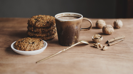 oatmeal cookies, brown mug with cocoa, walnuts, cinnamon, prunes, vintage spoon on the wooden tableの写真素材