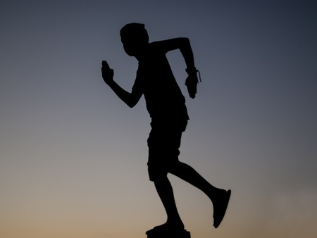silhouette of a person boy running towards sunset sky background. Man in shorts and tank top silhouette.の写真素材