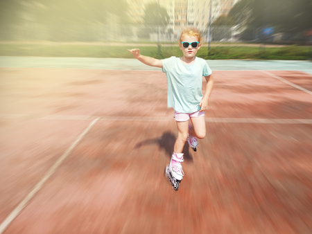 Little girl rides on rollers at a park on sunset.