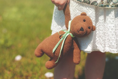 knitted toy in a knitted bag together with a bouquet of wild flowers in the hands of a little girl. Summer walk. Flower meadow.の写真素材