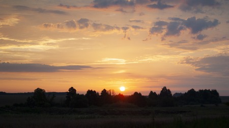 Beautiful blazing sunset landscape at over the meadow and orange sky above it. Amazing summer sunrise as a background. Beautiful dramatic twilight sunset Landscape with sun light shining through orange cloud over green fields.の写真素材