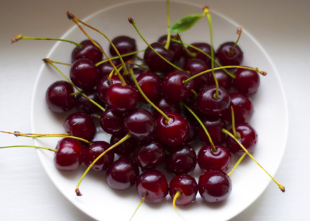 Cherries lie on a wooden table on a white dish under a tree in the open air in sunny weather.の写真素材