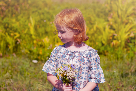 Cute cheerful redhead girl playing on the meadow, field. Beautiful little girl in the meadow near sunflowers and smiling. Soft sunlight.の写真素材