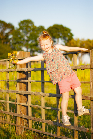 a child, a girl climbs a wooden fence in the village.の写真素材