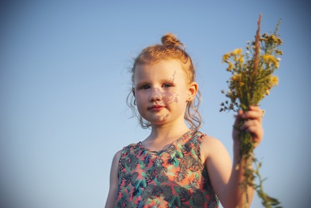 Happy young girl with a flower in his hand against the blue skyの写真素材