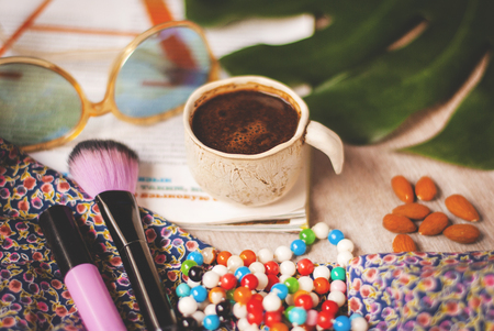 Layout, top view, cup of coffee, sunglasses, scarf, magazine, sheet of monstera, beads and makeup brush on a light background. Women's still life.の写真素材