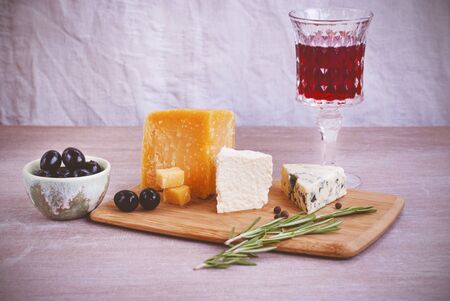 A glass of red wine, different types of cheese, olives, a sprig of rosemary.の写真素材