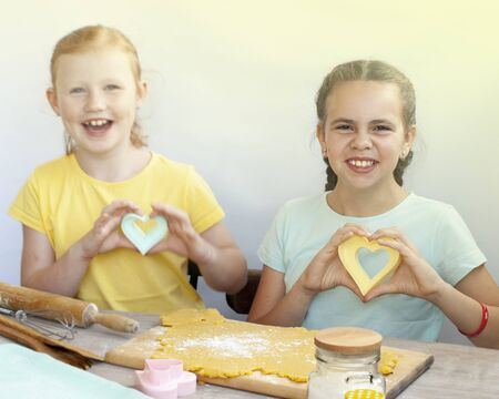 Two children a girl make cookies from dough. Two funny cheerful girls. Natural homemade food.の写真素材