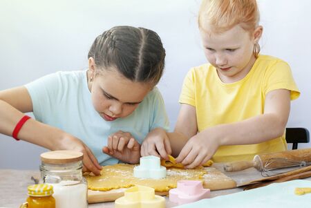 Two children a girl make cookies from dough. Two funny cheerful girls. Natural homemade food.の写真素材