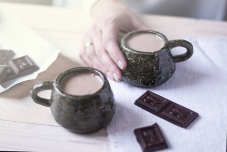 Woman hand holding a Cup of cocoa in the morning at home, next to a second Cup for a partner. Light background.の写真素材