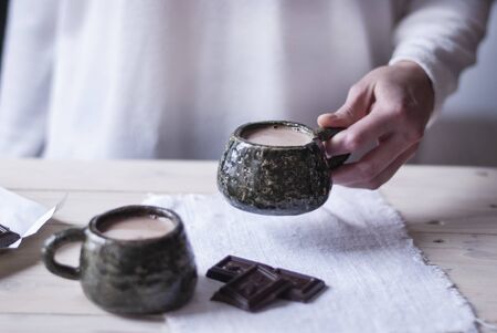 Woman hand holding a Cup of cocoa in the morning at home, next to a second Cup for a partner. Light background.の写真素材
