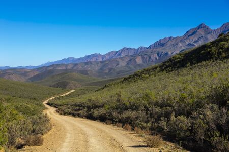 Gravel road next to the mountain rangeの写真素材