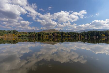 Clouds and autumn colored trees reflect on the waterの写真素材