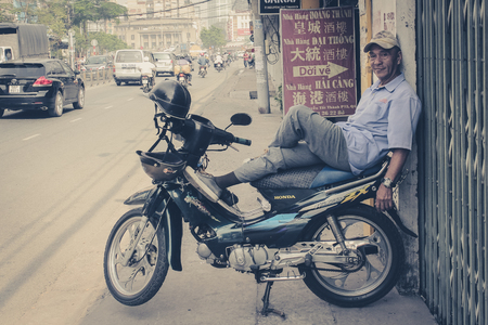 Saigon, Vietnam - January 17, 2014: Portrait of a man relaxing on his scooter / motorbike. Saigon is known as motorbike city.のeditorial素材