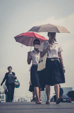 Bangkok, Thailand - March 05, 2014: Street portrait of two girls with umbrellas, one wearing a mask. Bangkok Air pollution reaches a critical level.のeditorial素材