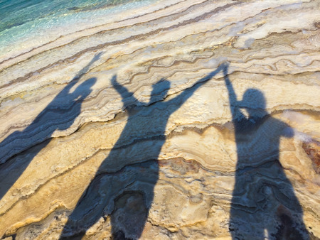 shadows of three happy people at beach raising hands -の写真素材