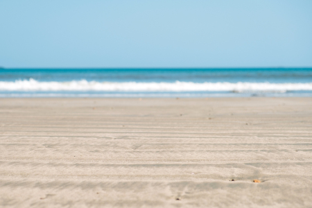 beach sand closeup with ocean wave and blue sky background