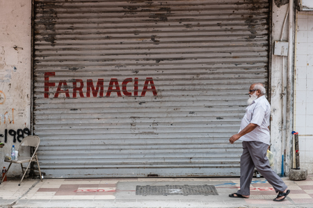 Old man walking on sidewalk in front of pharmacy on busy shopping street in Panama Cityのeditorial素材
