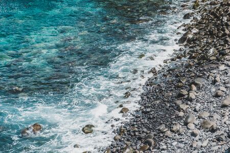 ocean waves on stone beach with black pebbles at rocky coast -の写真素材