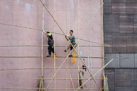 Hong Kong, November, 2019: Workers on construction site building bamboo scaffolding on house facade in Hong Kongのeditorial素材
