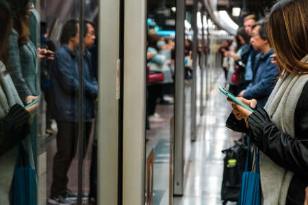 HongKong, China - November, 2019: Woman waiting for train looking on mobile phone at MTR station /...