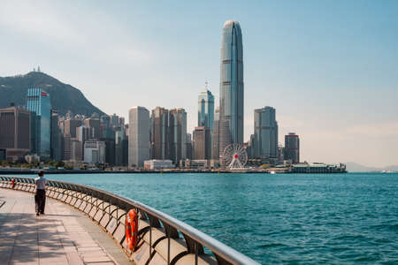 HongKong, China - November, 2019: Person walking at waterfront promenade with Victoria Harbor and skyline of Hong Kong Island in backgroundのeditorial素材