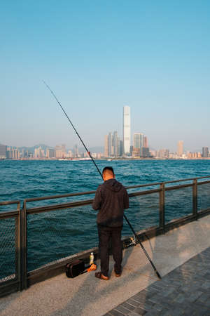 fisher man with fishing rod on coast with skyline of Hong Kong, Kowloonの写真素材