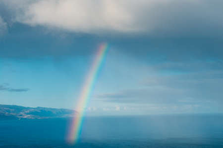 Rainbow coming out of cloud over ocean water -